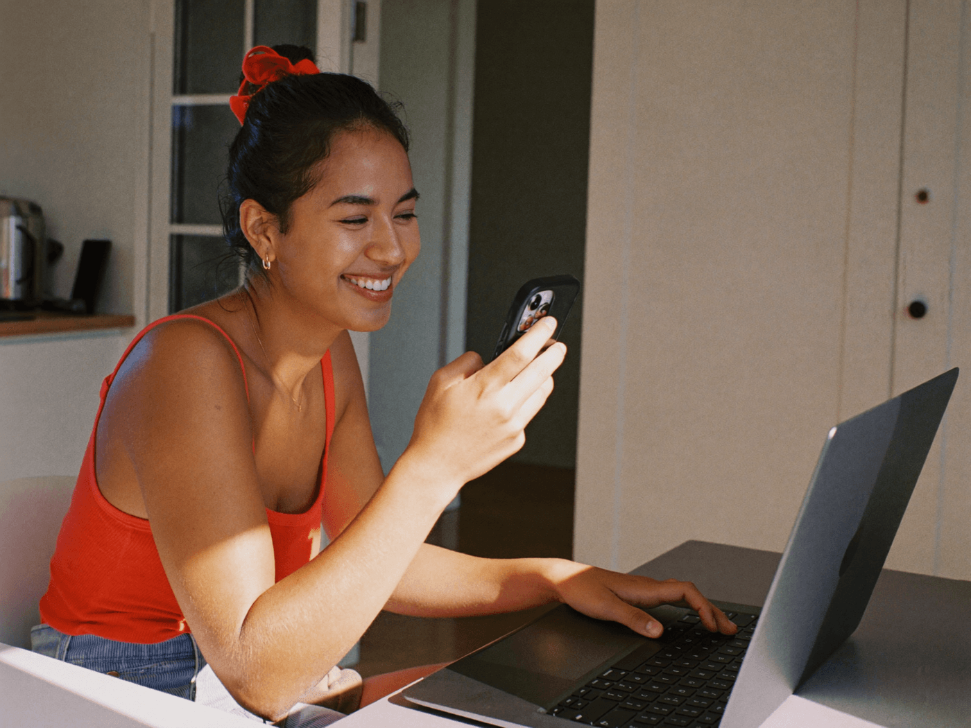 A smiling woman reviewing a loan application on her laptop and phone at home