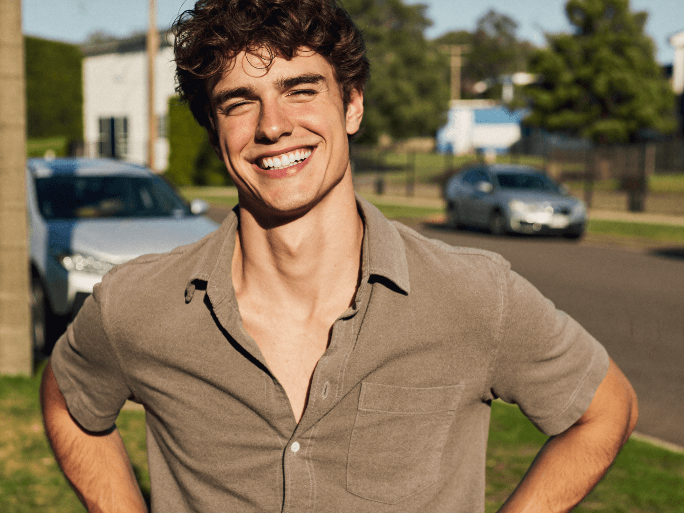 A cheerful young man smiling outdoors on a suburban street