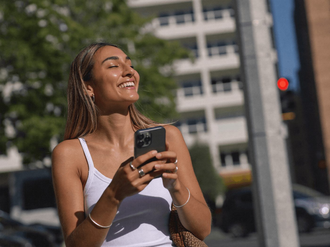 A smiling woman checking her phone on a sunny city street